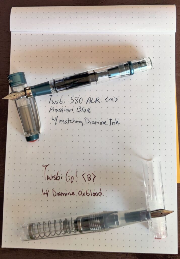 Twsbi 580 ALR in Prussian Blue and Twsbi Go in Clear on a notepad