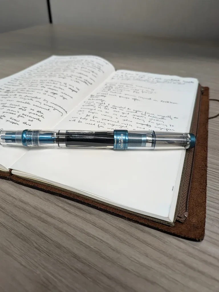 TWSBI Diamond 580 sits on an open spread of the 013 lightweight paper insert within a Travelers Notebook on a gray wood desk surface
